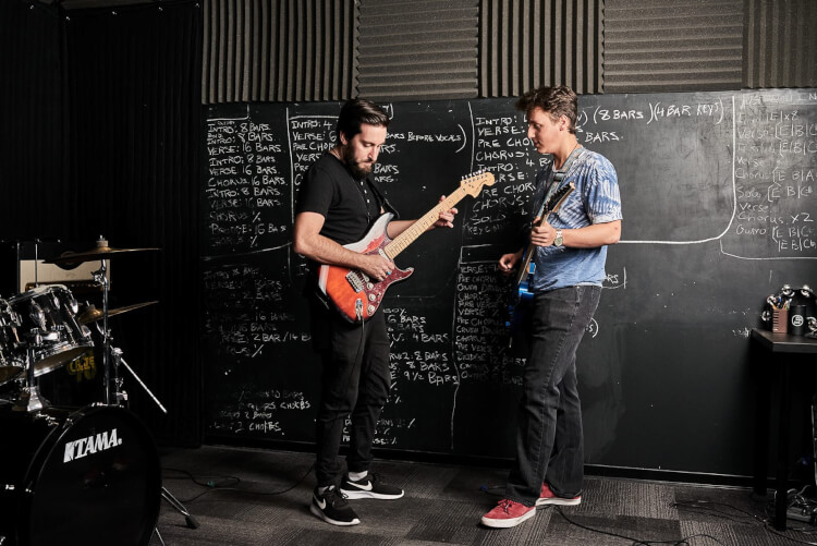 Instructor teaching advanced guitar lesson to a teenager